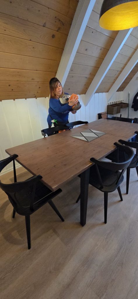Harbor Shores cleaner dusting a light fixture above a dining table in an A-frame cabin