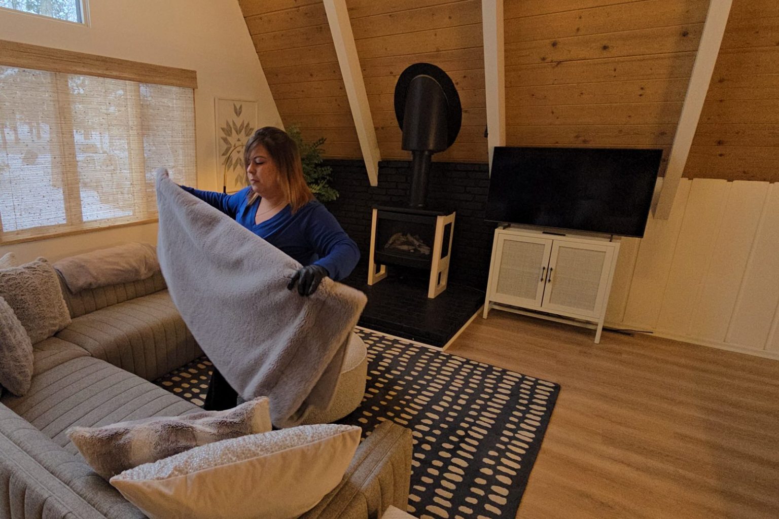 Harbor Shores cleaner folding a throw blanket in an A-frame cabin living room