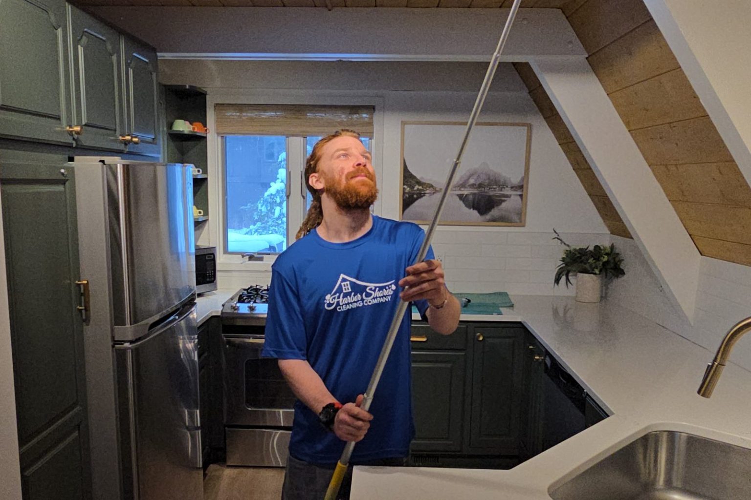 Harbor Shores cleaner dusting the kitchen ceiling with an extension pole duster
